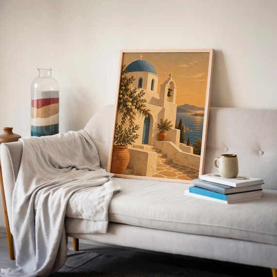 Santorini church wall art print leaning on a cream sofa against a beige wall beside books and a mug.