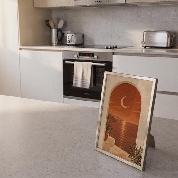 Mediterranean crescent moon arch print standing on a countertop in a modern white kitchen.