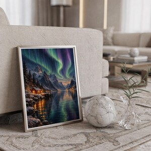 Aurora borealis mountain landscape wall art print in a silver frame leaning against a sofa beside a decorative marble sphere.