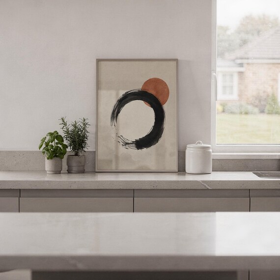 Framed minimalist black and red circle artwork standing on a shelf next to a city view window.