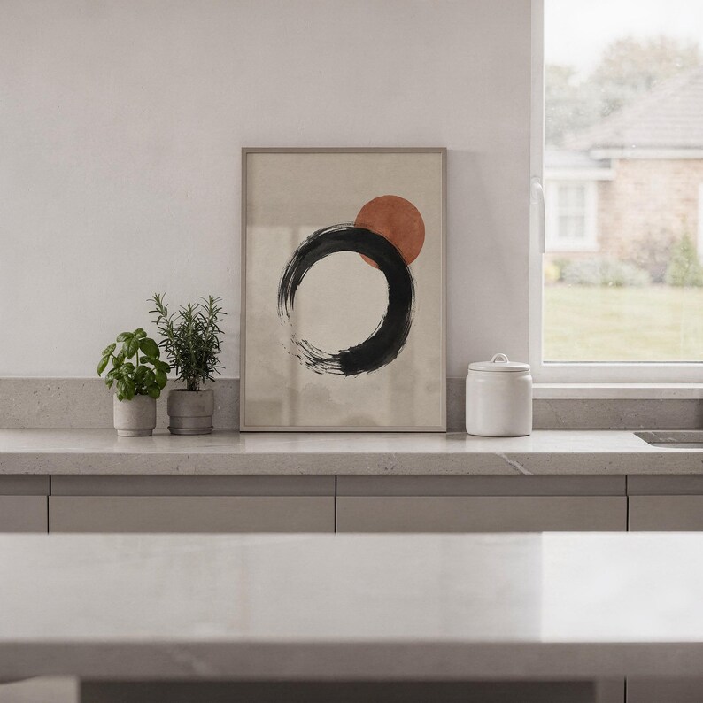 Framed minimalist black and red circle artwork standing on a shelf next to a city view window.