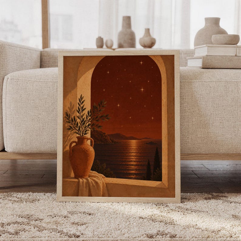 Mediterranean night sea wall art print featuring warm terracotta, burnt sienna, amber, and deep brown tones, a rustic arched window, olive branches in a clay vase, and a star-filled coastal horizon, framed and leaning against a beige sofa on a textured rug in a bright Scandinavian living room.