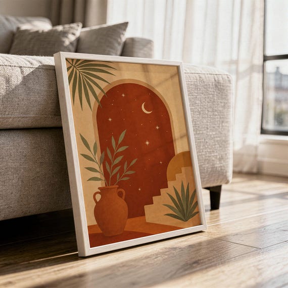 Terracotta moon and stars arch art print in a white frame leaning against a gray sofa on a sunlit wooden floor.