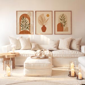 Set of 3 framed terracotta botanical wall art pieces hanging above a white sofa in a sunlit living room.