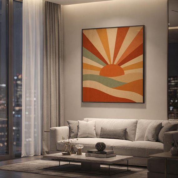 Retro geometric sunrise print showing a mid-century geometric sun with bold rays rising over rolling hills in terracotta, burnt orange, ochre and sage, hanging above a light gray sofa in a modern living room with evening city views through tall windows.