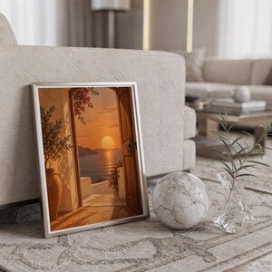 Mediterranean sunset doorway wall art print in a silver frame leaning against a sofa beside a decorative marble sphere.