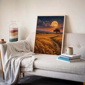 Moon wall art print leaning on a cream sofa against a beige wall beside books and a mug.