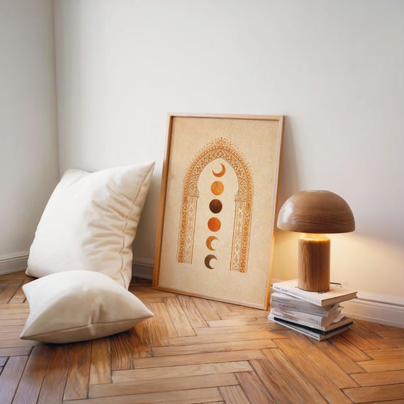 Japandi style terracotta moon phase poster resting on hardwood floor next to a modern table lamp and floor cushions⁠