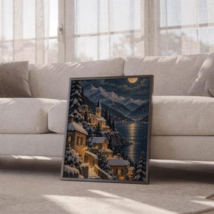 Snowy mountain village wall art print leaning against a white sofa in a bright living room with sheer curtains.