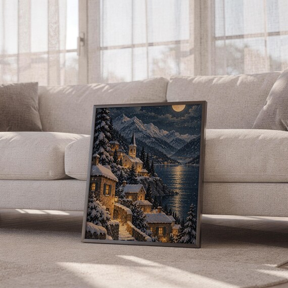 Snowy mountain village wall art print leaning against a white sofa in a bright living room with sheer curtains.