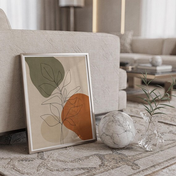 Framed botanical art leaning on the floor next to a white marble sphere in a bright room.