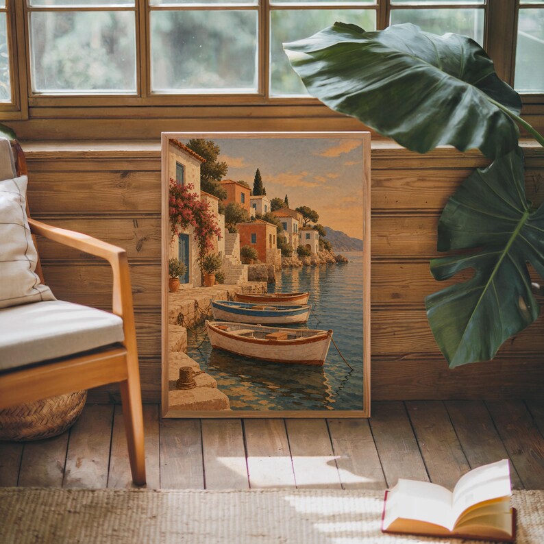 Mediterranean coastal village wall art print leaning against warm wood paneling beside a wooden armchair and a monstera plant.