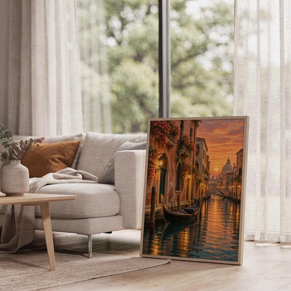 Venice canal sunset wall art print leaning on the floor beside a cream armchair next to large garden windows.