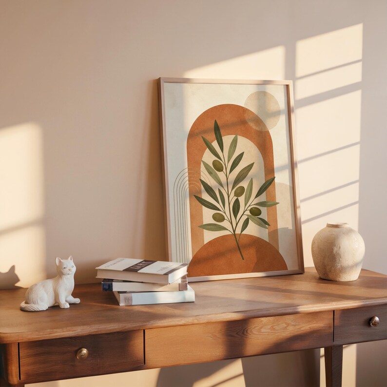 Olive branch art print on dark wooden desk with stacked books and sunlight