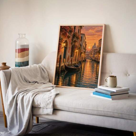 Venice canal sunset wall art print leaning on a cream sofa against a beige wall beside books and a mug.