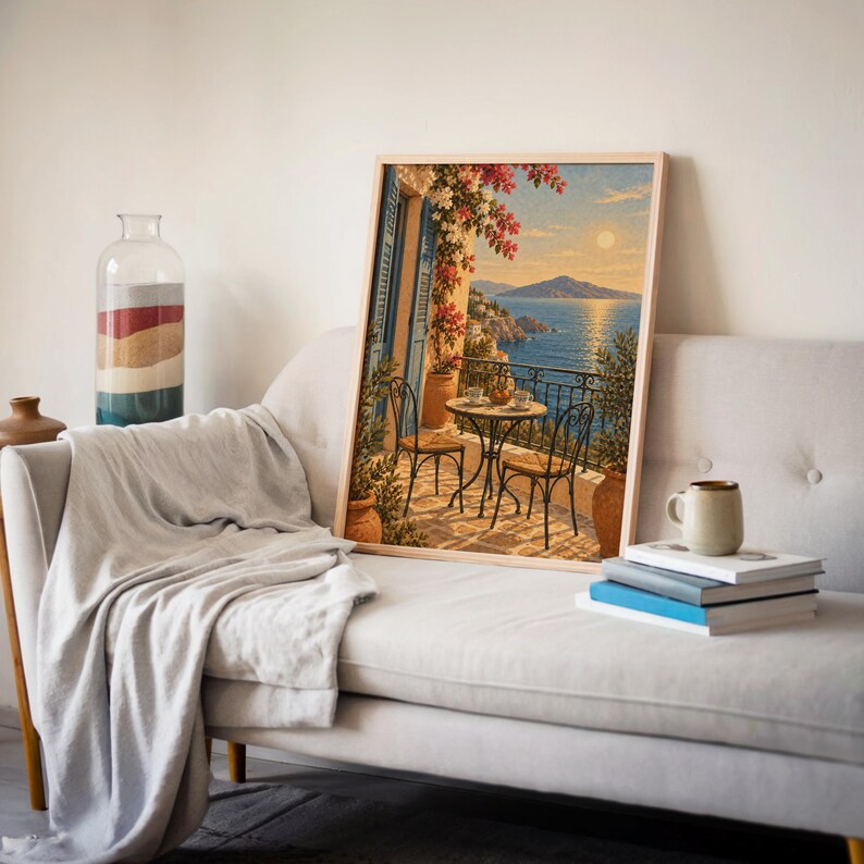 Mediterranean balcony wall art print leaning on a cream sofa against a beige wall beside books and a mug.