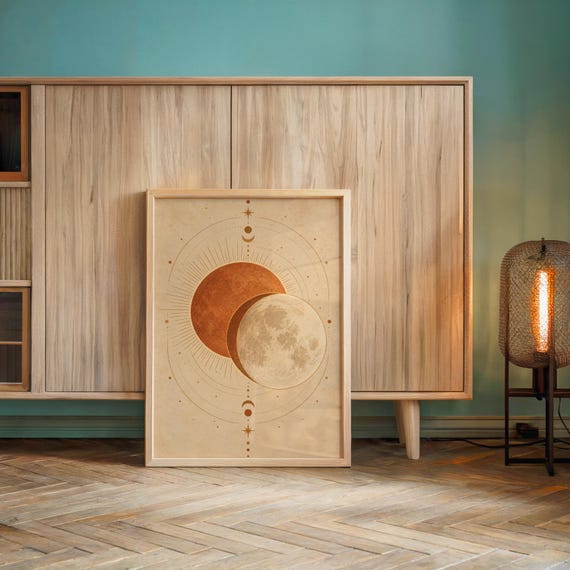 Sun and moon celestial wall art print leaning against a wooden cabinet by a teal wall beside a glowing floor lamp.