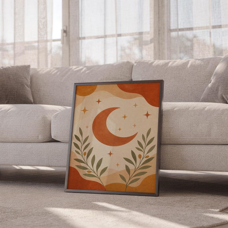 Terracotta crescent moon and olive branch print leaning against a white sofa in a bright living room with sheer curtains.