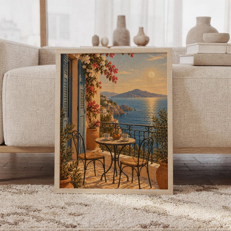 Mediterranean balcony wall art print featuring sun-warmed terracotta, soft cream, ocean blue, coral pink bougainvillea, and a serene sea view with distant mountains, framed and leaning against a beige sofa on a textured rug in a bright Scandinavian living room.