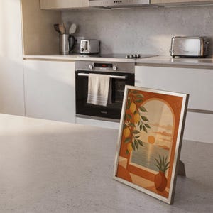 Mediterranean lemon and sea view arch print standing on a countertop in a modern white kitchen.