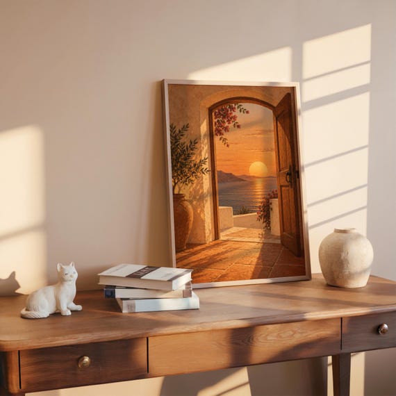 Mediterranean sunset doorway wall art print leaning on a wooden desk against a warm beige wall in soft window sunlight.