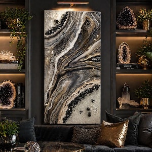 May include: Abstract wall art with a swirling design in black, white, and gold. The artwork is displayed in a dark room with shelves holding crystals and plants. A black sofa with gold cushions is in front of the art.