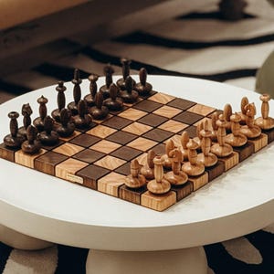 May include: A wooden chess set with dark brown and light brown pieces arranged on a checkered board. The chess pieces have a unique, stylized design. The board is set on a white table, with a black and white patterned rug in the background.