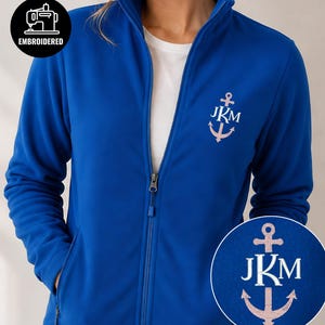 Puede incluir: Una chaqueta polar azul real con cremallera y un diseño de ancla bordado en blanco en el pecho izquierdo. El gráfico del ancla incluye las letras JKM en texto blanco. Una insignia circular en la esquina superior izquierda muestra el texto EMBROIDERED.