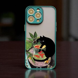 以下が含まれることがあります： 赤い魚が入った金魚鉢に手を伸ばす黒猫が描かれた、ティールとクリアの携帯電話ケース。ケースには、3つのカメラレンズとフラッシュを備えたティール色のカメラバンプがあります。デザインには、緑の葉と水彩画風の背景が含まれています。