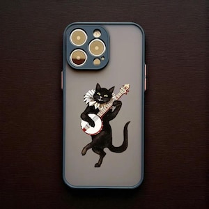以下が含まれることがあります： バンジョーを演奏する黒猫のイラストが描かれた携帯電話ケース。猫はフリルカラーを着用しています。ケースはグレーの背景、青い縁取り、金色のディテールが施されたカメラモジュールを備えています。