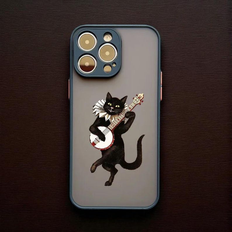 以下が含まれることがあります： バンジョーを演奏する黒猫のイラストが描かれた携帯電話ケース。猫はフリルカラーを着用しています。ケースはグレーの背景、青い縁取り、金色のディテールが施されたカメラモジュールを備えています。