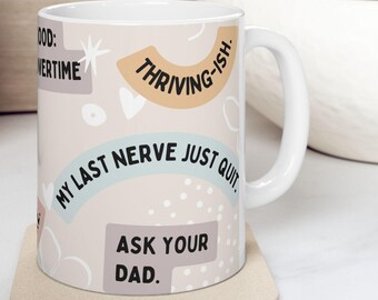 May include: White ceramic mug with the phrases "MY LAST NERVE JUST QUIT" and "ASK YOUR DAD" in black text. The mug also features the text "THRIVING-ISH" and "OVERTIME". The mug is on a beige coaster.