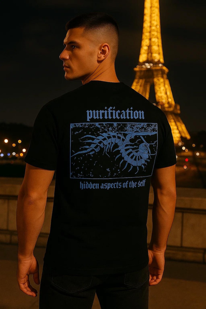 Puede incluir: Camiseta negra con un gr&aacute;fico azul y texto en la espalda. El texto dice "purification" encima de una ilustraci&oacute;n azul de una criatura, con "hidden aspects of the self" debajo. La Torre Eiffel est&aacute; al fondo.
