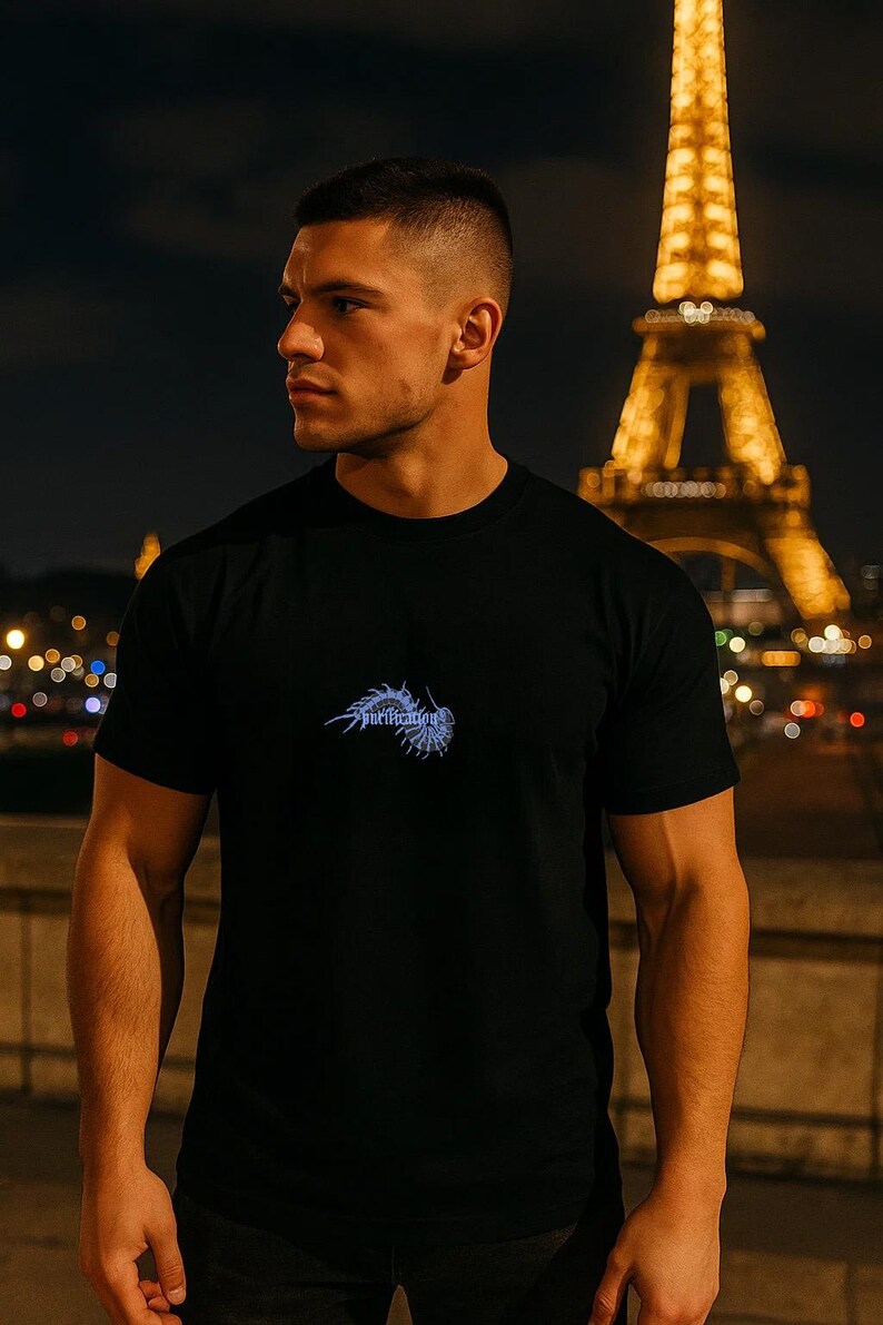 Puede incluir: Camiseta negra de cuello redondo con un dise&ntilde;o gr&aacute;fico azul en el pecho. La Torre Eiffel es visible al fondo, iluminada por la noche. La palabra "Purification" forma parte del gr&aacute;fico.