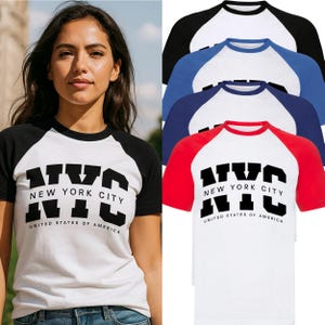 Könnte beinhalten: Weiße T-Shirts mit schwarzen, roten und blauen Raglanärmeln, jeweils mit dem schwarzen Schriftzug "NYC New York City United States of America". Die Shirts sind gestapelt.
