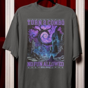 May include: Dark gray t-shirt featuring a fantasy scene with a swirling purple tree and a figure in a hooded cloak. Text on the shirt reads "TURN 2 COMBO" and "NO FUN ALLOWED". The design is framed by a purple border.
