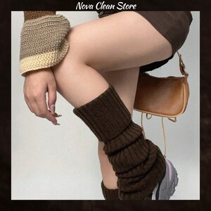 May include: Brown leg warmers made of a ribbed knit material. The leg warmers are worn with a pair of sneakers. The image also shows a brown purse and a sleeve of a sweater.