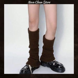 May include: Brown knitted leg warmers with a ruffled edge, worn over black patent leather shoes. The leg warmers are a dark brown color and have a ribbed texture. The shoes have a chunky sole and decorative buckles.