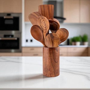 Peut inclure: Ensemble d'ustensiles de cuisine en bois, comprenant des cuillères et une spatule ajourée, présentés dans un support en bois assorti. Les ustensiles sont en bois aux tons chauds, et le support est cylindrique. L'arrière-plan montre une cuisine.