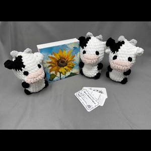 Peut inclure: Trois figurines de vache au crochet faites à la main, avec des motifs noirs et blancs, des cornes grises et des museaux roses. Une petite peinture d'un tournesol et deux cartes sont également dans l'image. Les vaches sont un objet décoratif charmant et fantaisiste.