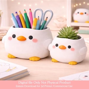 May include: Two white ceramic chick-shaped containers. One holds pencils and scissors, the other a small succulent plant. Both have orange beaks, black eyes, and pink cheeks. Yellow feet complete the design. The containers are on a light-colored surface.