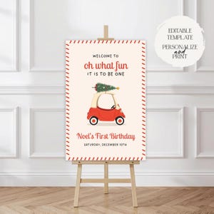 以下が含まれることがあります： イーゼルに立てられた誕生日のサイン。赤い車とクリスマスツリーのイラストが特徴です。「Welcome to oh what fun it is to be one」と「Noel's First Birthday, Saturday, December 10th」と書かれています。テンプレートは編集可能です。