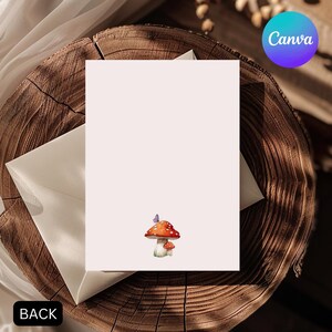 May include: A blank card with a watercolor illustration of two mushrooms and a butterfly. The card is light pink and has the word "BACK" in the lower left corner. The Canva logo is in the upper right corner. The card is placed on a wooden surface.