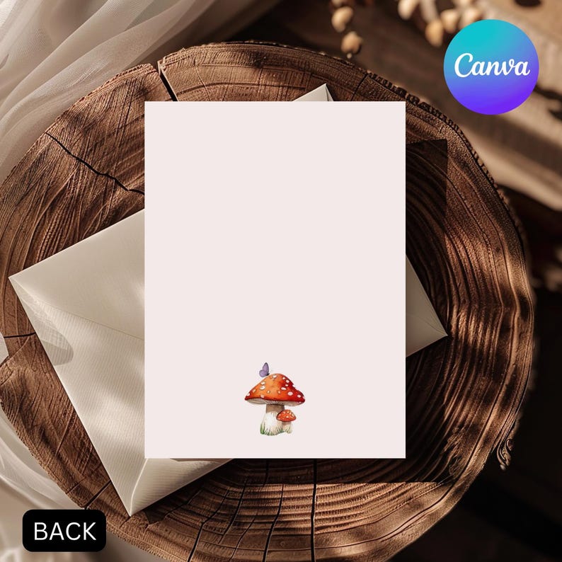 May include: A blank card with a watercolor illustration of two mushrooms and a butterfly. The card is light pink and has the word "BACK" in the lower left corner. The Canva logo is in the upper right corner. The card is placed on a wooden surface.