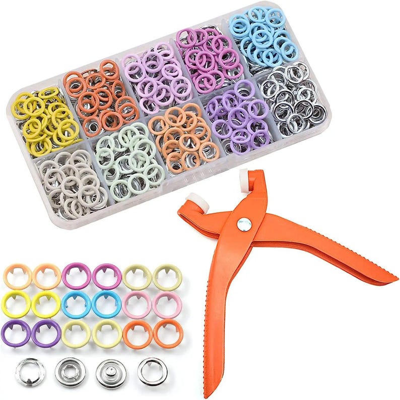 May include: A craft kit featuring a variety of colorful eyelets in a clear plastic organizer. An orange hand tool is also included. The eyelets are in shades of yellow, orange, pink, purple, blue, and silver.
