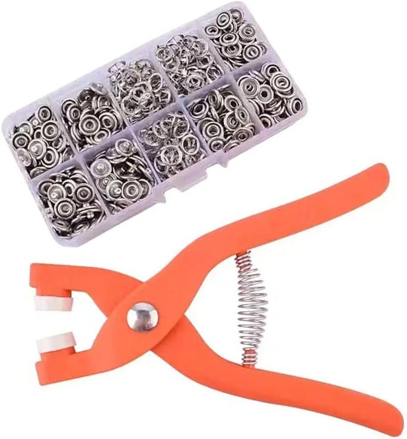May include: An orange snap fastener tool with a silver spring and a clear plastic organizer filled with silver snap fasteners. The organizer is divided into compartments, each containing a different quantity of snaps.