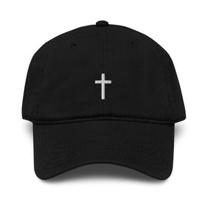 Könnte beinhalten: Schwarze Baseballkappe mit gebogenem Schirm und verstellbarem Riemen. Ein kleines, weiß gesticktes Kreuz ist mittig auf der Vorderseite. Die Kappe ist aus einem weichen, strapazierfähigen Stoff gefertigt.
