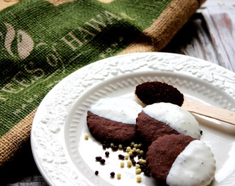 May include: Four chocolate cookies with white icing on a white plate with a brown and green hessian background. The cookies are arranged in a circle with a spoon of coffee grounds in the centre.