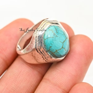 Könnte beinhalten: Ein silberner Ring mit einem großen, ovalen Türkisstein. Der Stein hat ein Rissmuster und ist in einem strukturierten Metallband gefasst. Der Ring wird in einer Hand gehalten, mit dem Text "Sai Jewelry Crafts" sichtbar.