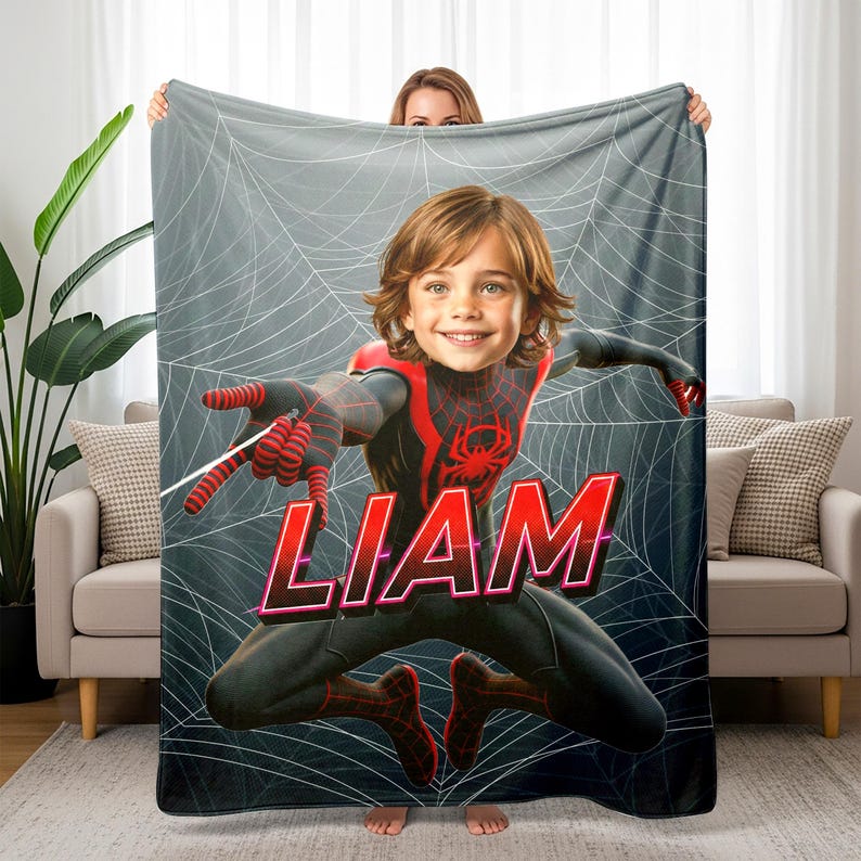 Peut inclure: Une couverture personnalis&eacute;e avec le visage d'un enfant superpos&eacute; &agrave; un costume inspir&eacute; de Spider-Man. La couverture a un fond gris avec un motif de toile d'araign&eacute;e blanche. Le nom "LIAM" est affich&eacute; en grandes lettres rouges.